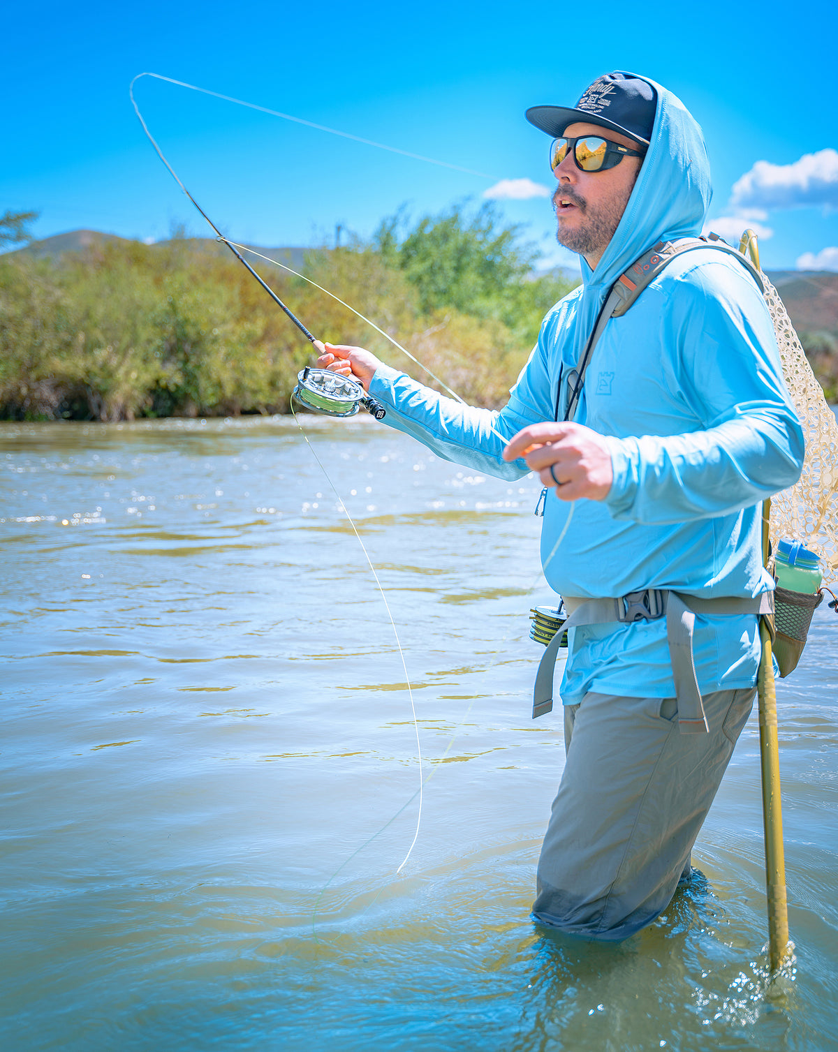 Angler fighting a fish with a Hardy Firecrest fly rod while wading in a river.
