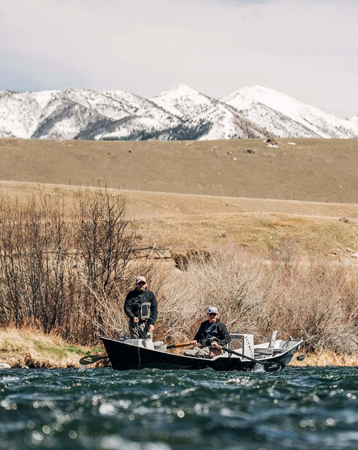 Fly anglers drifting a river beneath snow-capped mountains on a Hardy fly fishing trip.