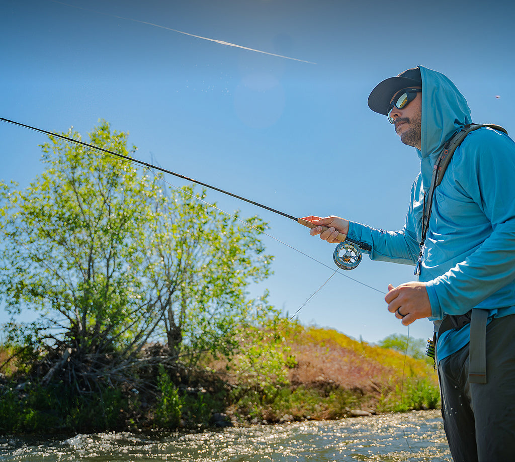 Angler fly fishing with a Hardy Firecrest fly rod in a scenic mountain landscape.