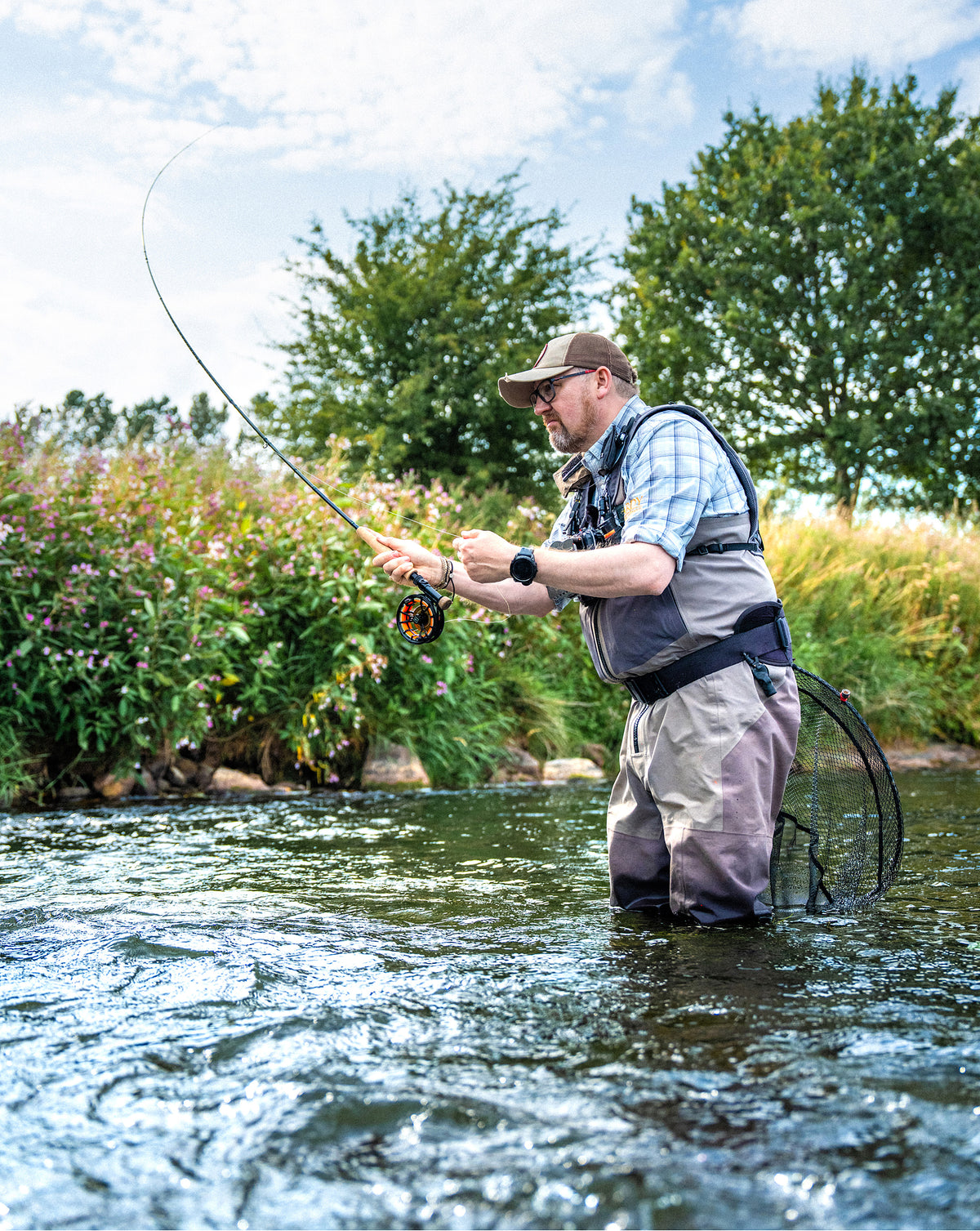 Angler fly fishing with a Hardy Tactus rod and reel while wading in a river.