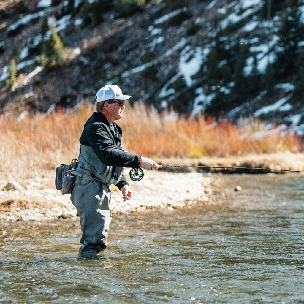 Man fly fishing in a river with a mountainous background