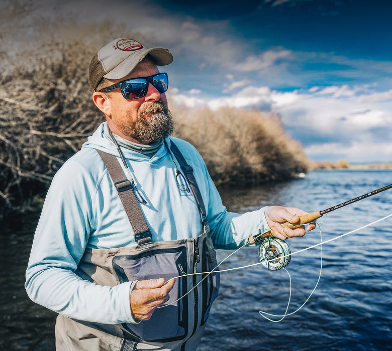 Man fly fishing by a body of water with a scenic background